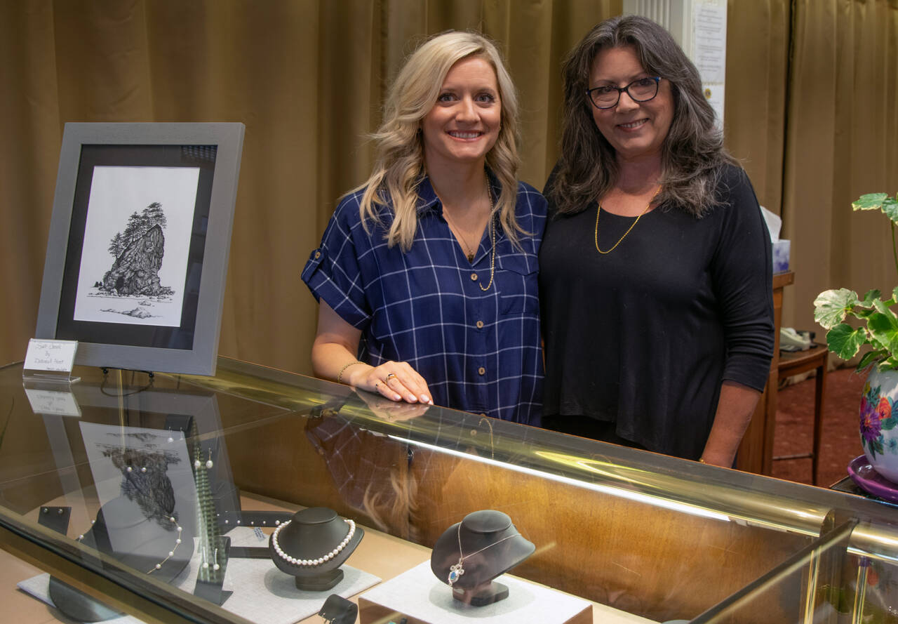 Libby Rogers and Debbie Hunt smile from behind one of the jewelry cases at Cole’s Jewelers, which they re-opened this June after the previous owners retired last year. Cole’s sells the designers locals have come to expect, and incorporates the same values as the previous Cole’s, but also has a few new elements, such as the pen and ink prints of drawings by Hunt, one of which can bee seen beside Rogers. Sequim Gazette photo by Emily Matthiessen