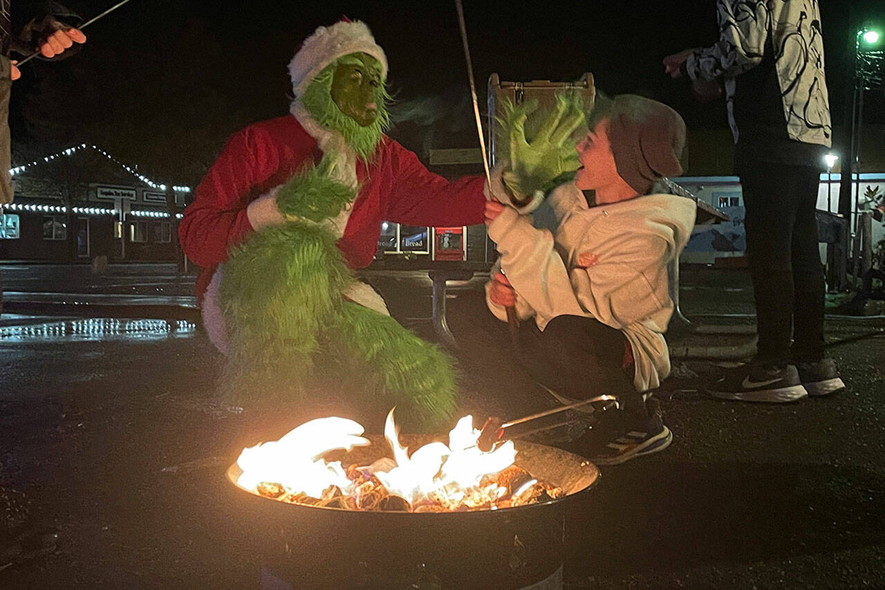 Sequim Gazette photo by Matthew Nash/ The Grinch (Brandon Tucker, a volunteer firefighter with Clallam County Fire District 3) says hello and surprises Connor Horst as he and other helper elves cook hot dogs on Dec. 9 on the last night of Santa’s Toy and Food Fire Brigade event that collected donations for Sequim Community Aid and Sequim Food Bank.
