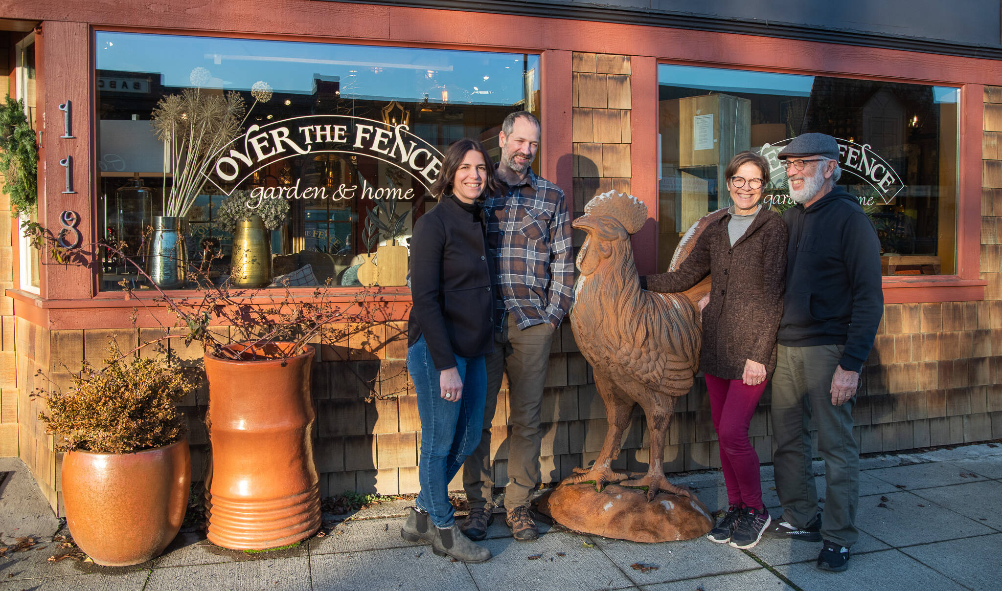 Sequim Gazette photo by Emily Matthiessen / Emily Underwood stands with her husband Scott Underwood, left, and her parents Jeri and Fran Sanford stand on the other side of Over the Fence’s giant metal rooster. The end of 2022 marks the transition of ownership of the store between the two couples.