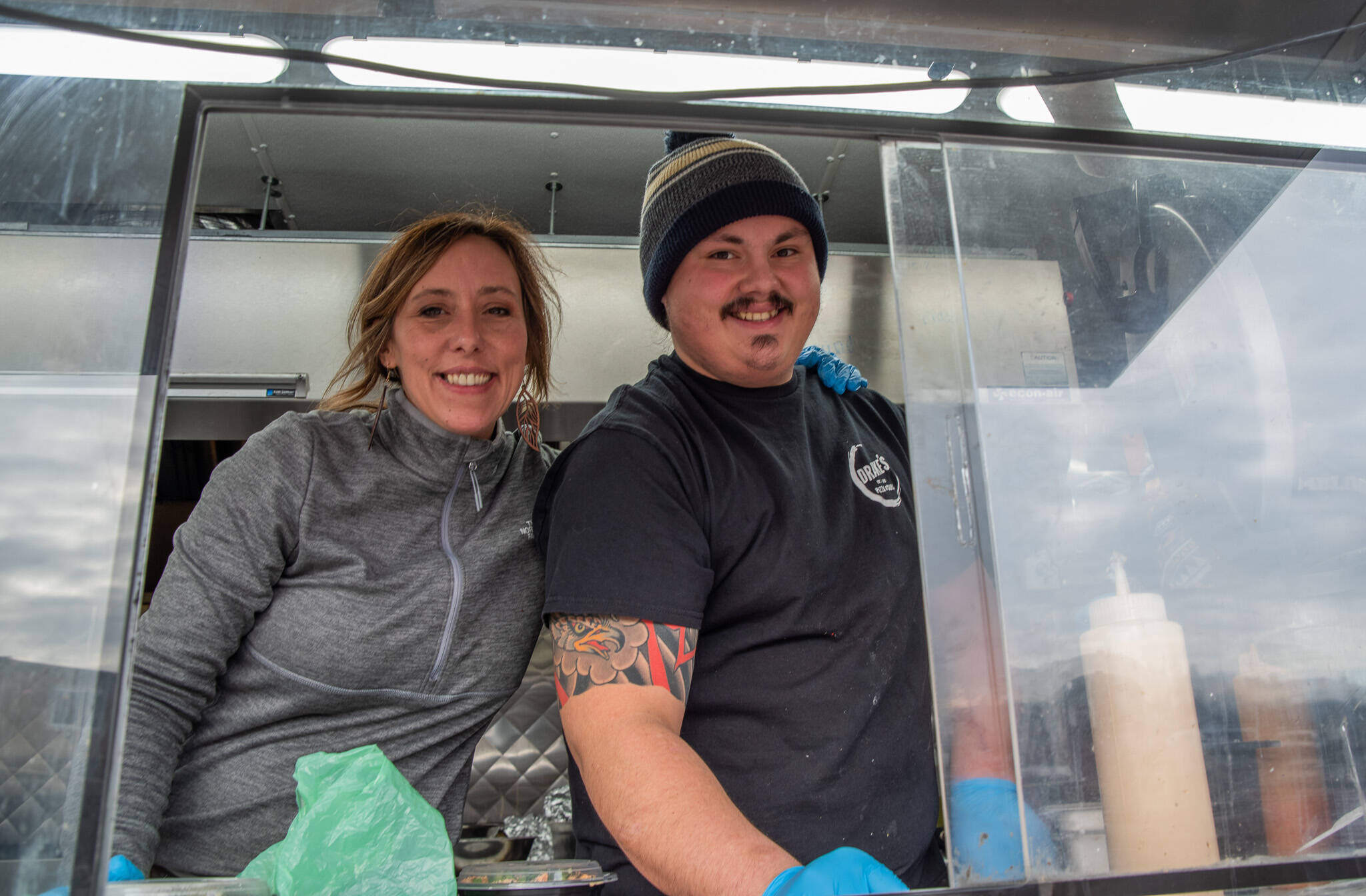 Sequim Gazette photo of Emily Matthiessen / Opal Joy Ruddock and her son Max Unruh, take the customer out the window of the Da Kindz Island Grill food truck.