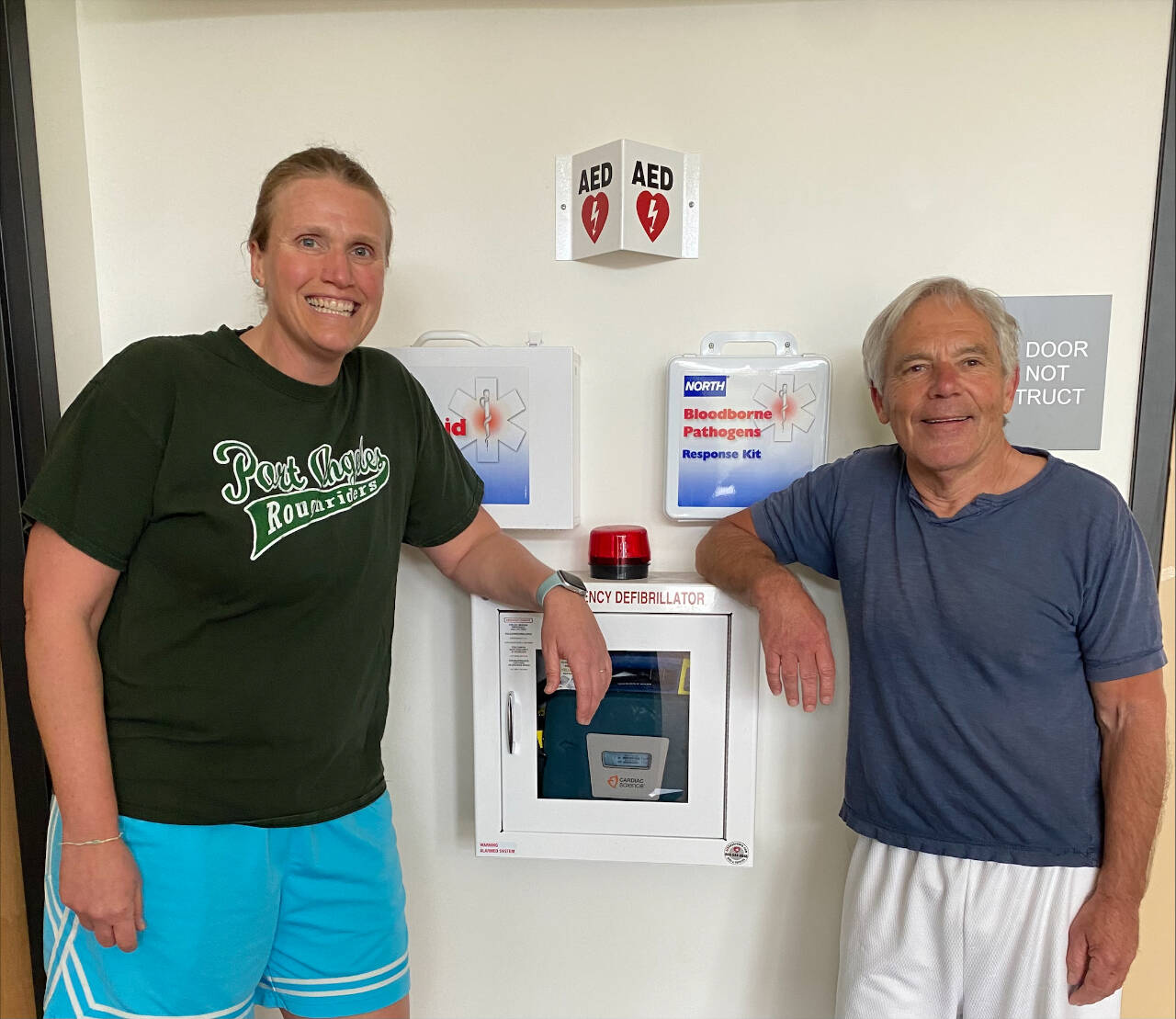 Photo courtesy of Peninsula College / Allison Mahaney and Mike Aldrich are pictured near an Automated External Defibrillator (AED) device at Peninsula College. The pair gave CPR to fellow “Noon Hoops” teammate Bob Lawrence after he collapsed on the court.