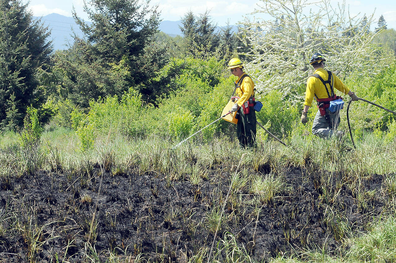 Photo by Keith Thorpe/Olympic Peninsula News Group / Clallam County Fire District 2 firefighters Chris Dalen, left and Zach Gear put out hot spots around the perimeter of a brush fire near 2333 Lower Elwha Road in May. Dry conditions in the region have led to burning restrictions in Clallam County and Jefferson County.