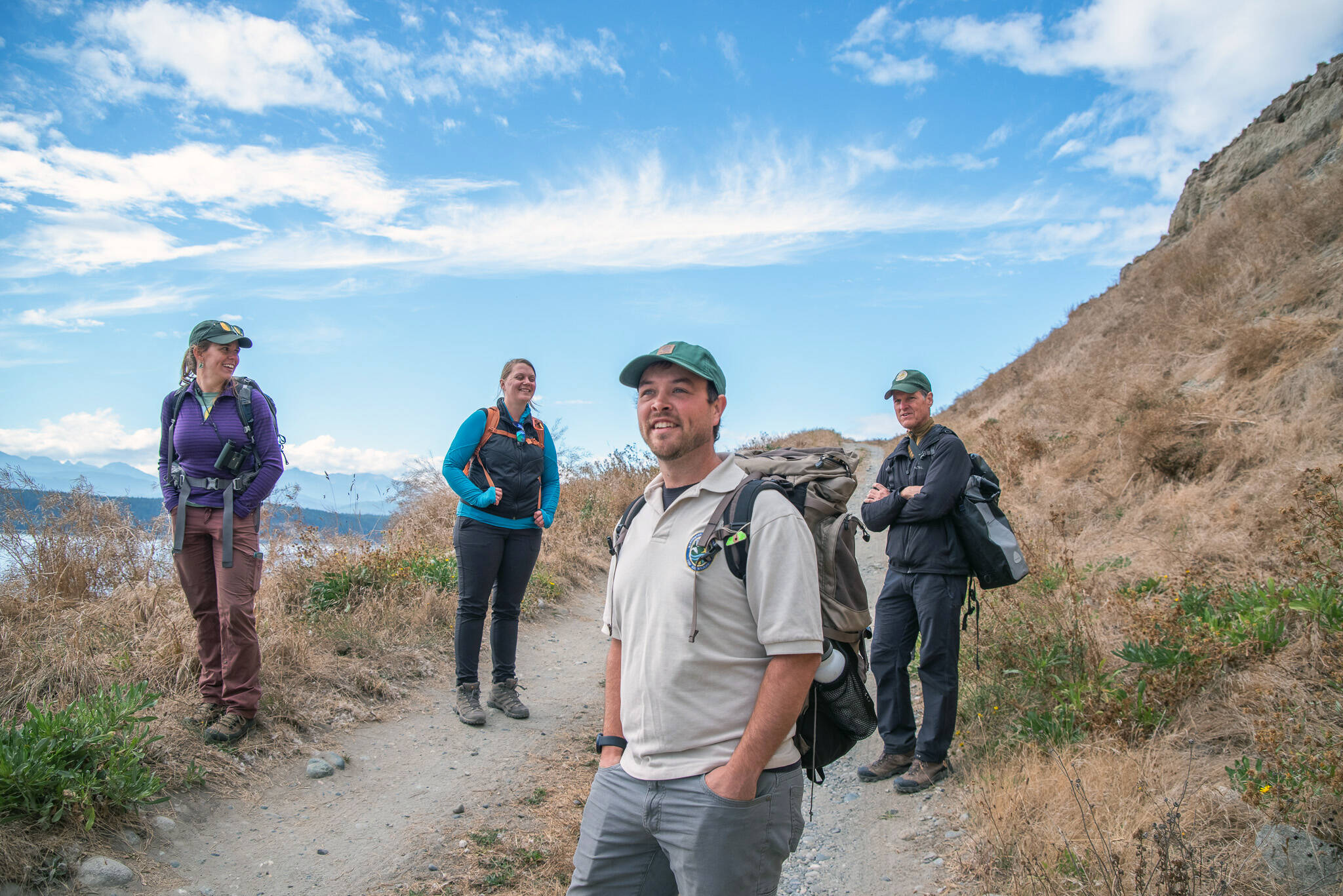 Senior Research Scientist Scott Pearson, right, leads a team from Washington State Fish and Wildlife on a tour along the road through Protection Island to a viewpoint of where the Aug. 3, 2021, fire burned through 26 acres, primarily on state protected land known as the Zella M. Schultz Seabird Sanctuary. From left, Katie Laushman, WDFW wildlife area manager, Samantha Montgomery, division manager, and Josh Cook, prairie restoration specialist, take in the view. Laushman and Cook are part of an effort to reseed burned areas with native plants.