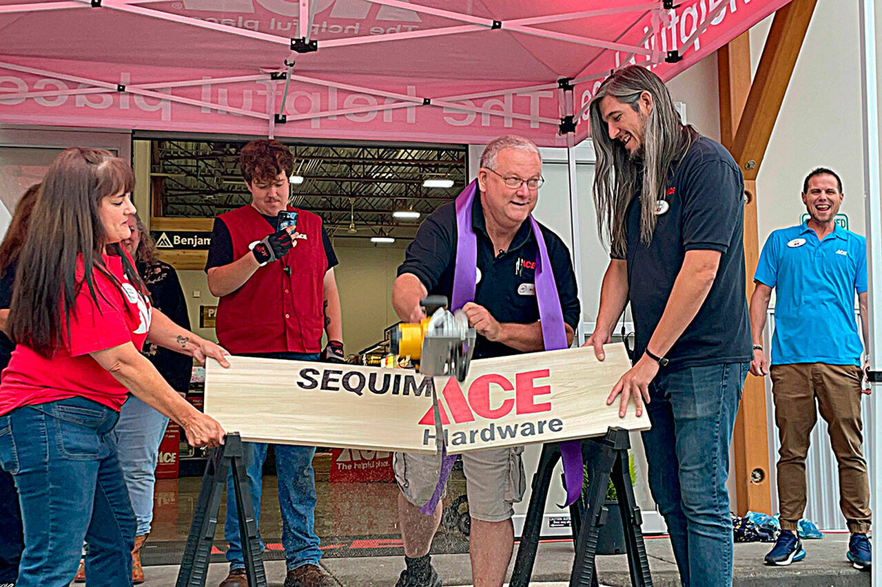 Sequim Gazette photo by Matthew Nash
Store manager Bill McClansburgh saws a sign in half on Aug. 31 to commemorate the grand opening of Sequim Ace Hardware.
