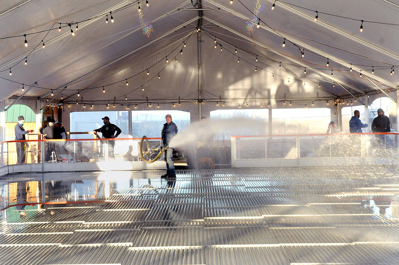 KEITH THORPE/PENINSULA DAILY NEWS
Tommy Robertson of Port Angeles, center, sprays water onto chiller coils that will eventually create the ice skating surface at the Port Angeles Ice Village on Tuesday in downtown Port Angeles.