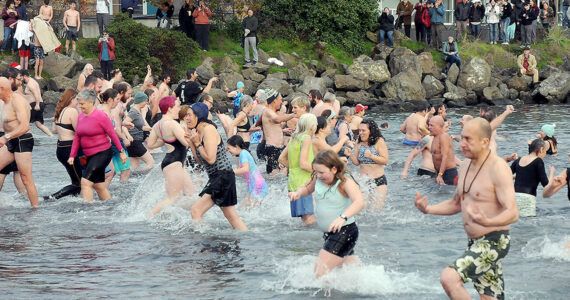 Participants in the New Year's Day polar bear dip in Port Angeles run in and out of the chilly water of Port Angeles Harbor at Hollywood Beach as onlookers watch from the shore on Monday. More than 100 dippers took part in the annual ritual, which served as a fundraiser for Volunteer Hospice of Clallam County. (Keith Thorpe/Peninsula Daily News)