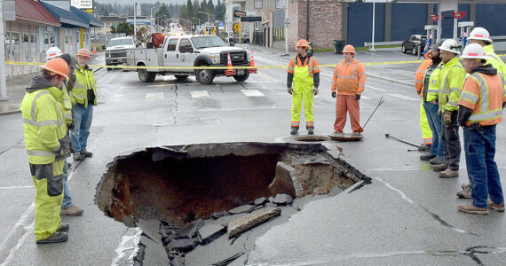 Port Angeles Public Works and Washington State Department of Transportation officials examine a sinkhole in the middle of Fifth and Lincoln streets in Port Angeles on Wednesday after water from a broken water main tore up the pavement. (Keith Thorpe/Peninsula Daily News)