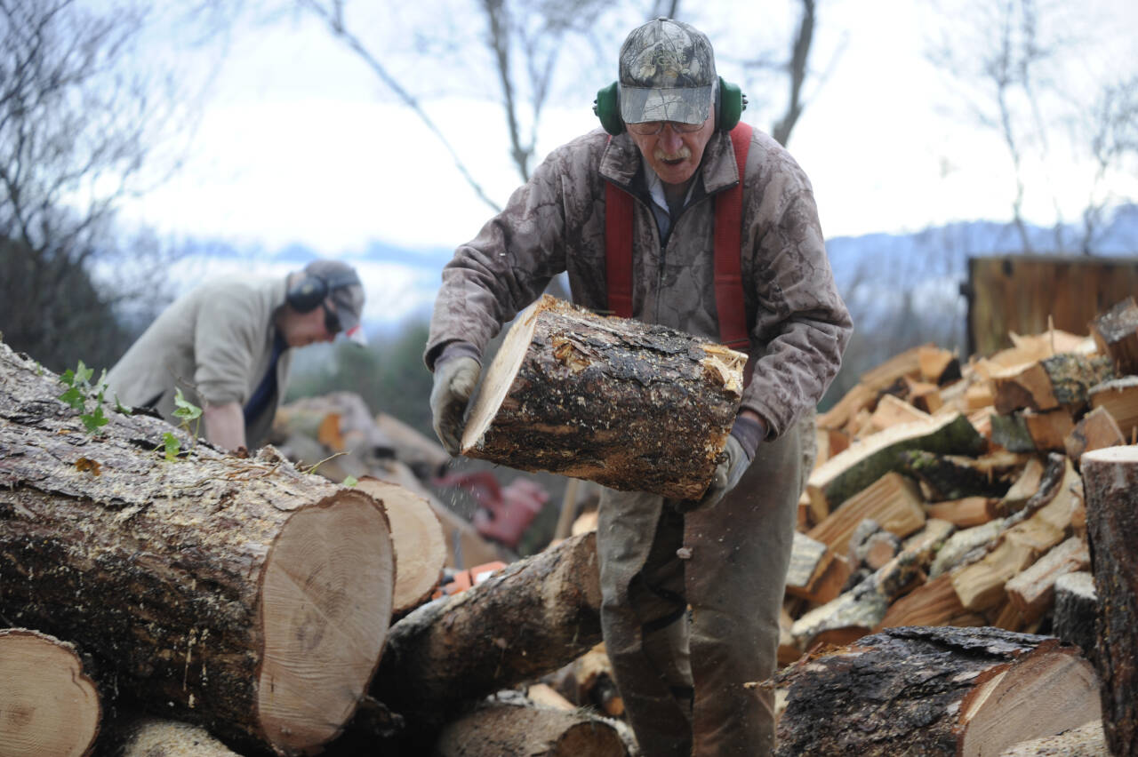Sequim Gazette photo by Michael Dashiell / Wally Jenkins tosses a piece of wood into a pile as he and fellow woodcutters compile cords of firewood to sell, using the funds for the Path From Poverty nonprofit.