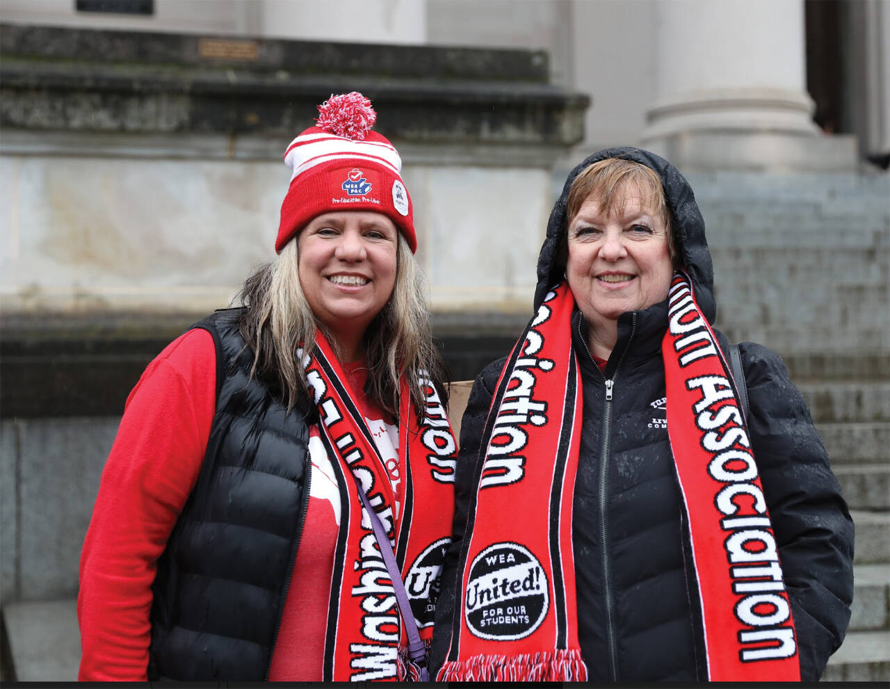 Photo by Mary Murphy/Washington State Journal / Melissa Walker, paraeducator, left, and Terry Winkler, a fifth-grade teacher, sport Washington Education Association gear as they rally in the rain for fair wages on Feb. 19.