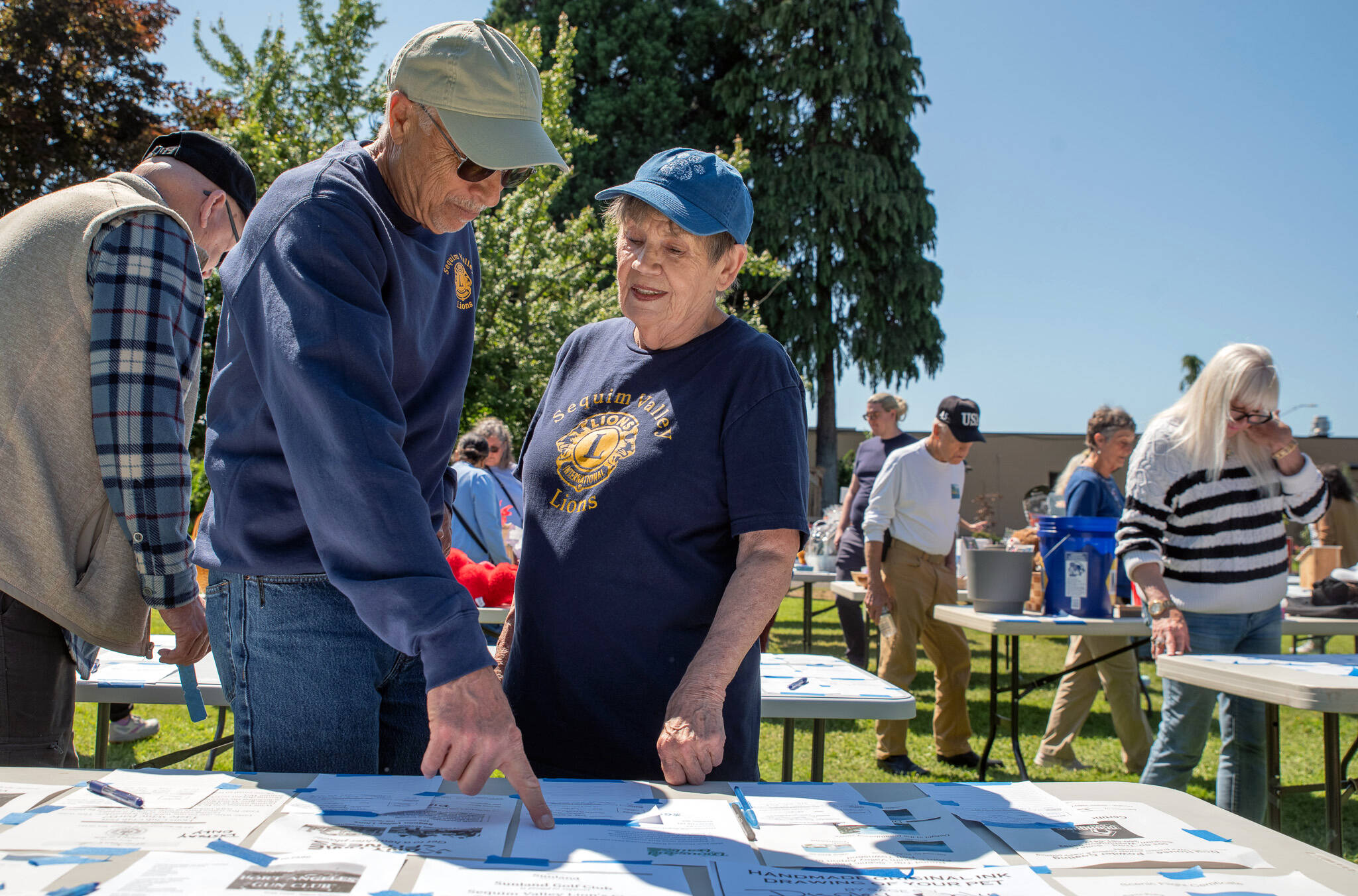 Sequim Gazette photo by Emily Matthiessen / Jeff Brown, left, and Sandra Granun discuss silent auction items at the Sequim Valley Lions’ 12th Annual Crab feed held in Pioneer Park on Saturday. There was an outpouring of support from local businesses resulting in a large amount of items in the auction, many of which were won at a low price by attendees. The Lions use everything beyond costs of charity, according to new member Brown, including such things as building handicap ramps for people who can’t afford them, which he said is the reason he joined the nonprofit. “The things we contribute to, it’s phenomenal,” Brown said.