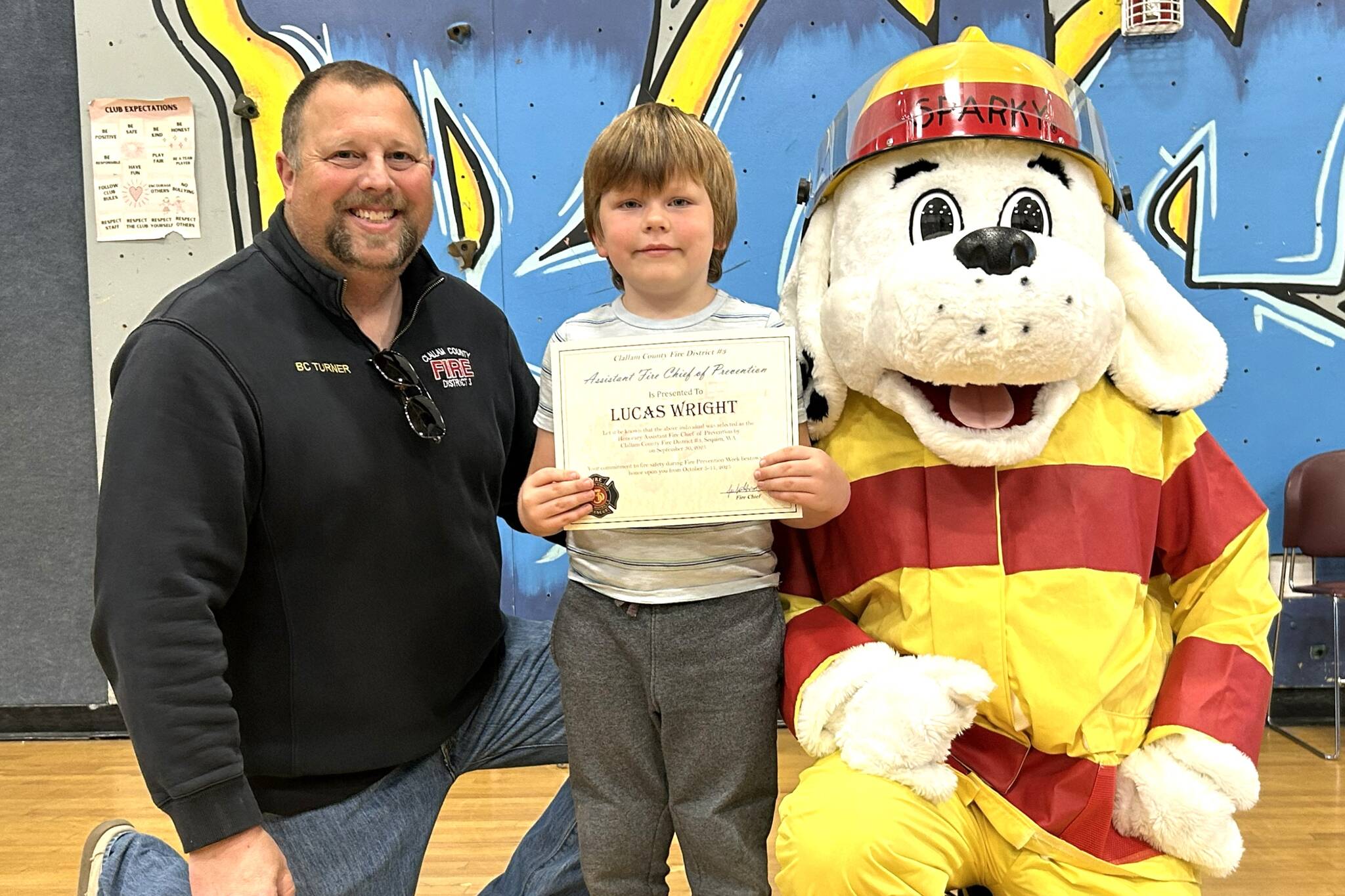 Sequim Gazette photo by 
Matthew Nash
Lucas Wright stands next to Battalion Chief Chris Turner and Sparky the Fire Dog after receiving a firefighter action figure prize and a certificate naming him honorary assistant fire chief of prevention during Fire Prevention Week, Oct. 5-11. Lucas won a coloring contest sponsored by the Sequim Gazette with Hi-Way 101 Diner and CCFD3 as partners.