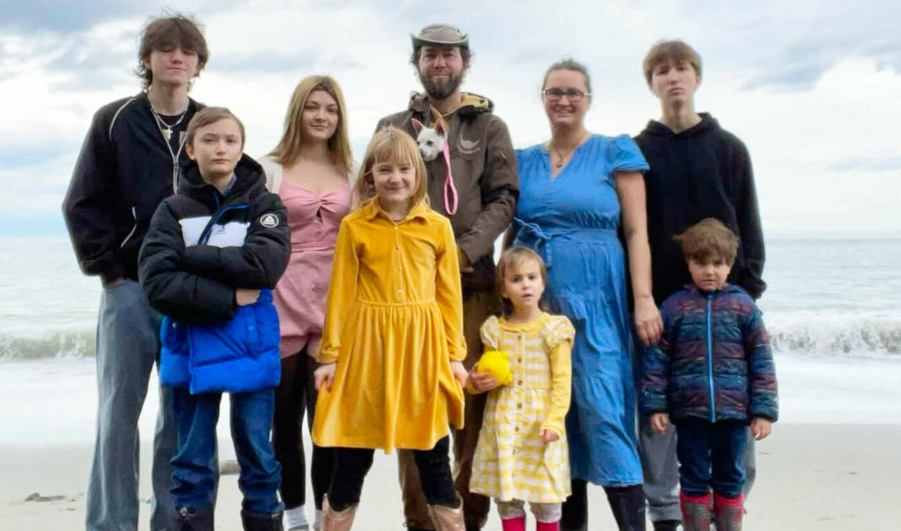 Photo courtesy Cindy Sylvester
Joshua and Cindy Sylvesters brood includes five biological sons, two of whom are grown, a teen girl who needed a home, a 9-year-old whom they adopted through the Indian Child Welfare Act, and two younger children who came to them through kinship foster care. The couple asked that the teen girl and three younger children not be fully named. Shown left to right are: Azuriah Sylvester, Zishe Sylvester, Taylor S., H Sylvester, Joshua Sylvester (holding family dog Queso), R, Cindy Sylvester, Phin Sylvester, and O.