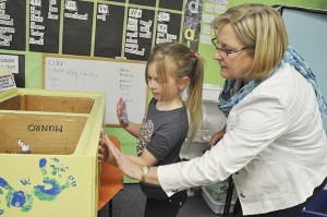 Teacher Renee Mullikin helps Ryleigh Miller apply the correct amount of pressure while creating hand-printed flowers. The wooden boxes