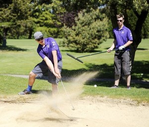 Jade Arnold shoots his way successfully out of the sand pit at hole No. 7 with Alex McCracken behind him at The Cedars at Dungeness against Klahowya.