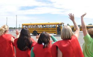 Teachers and other staffers from Helen Haller Elementary School — some dressed as apples — wave goodbye to students on the final day of school on June 18. Youths are on summer break until the 2015-2016 school year starts on  Sept. 1.