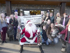 Olympic Peninsula Equine Network founders Valerie Jackson and Diane Royall (in tan T-shirts) celebrate on Dec. 19 with Santa (Mac Macdonald) and members of the Silver Spurs 4-H Club. The club raised $650 to buy a pallet of senior horse feed from the Co-op Farm & Garden for the horses that OPEN cares for. As part of the festivities