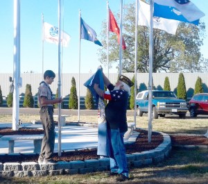 Carlsborg VFW member Larry Klinefelter and Boy Scout Braven Headley raise the new flags in front of the Sequim Museum & Arts recently. The 11 flagpoles have been empty since the death of museum treasurer Louie Rychlik
