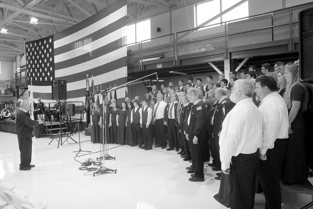 A combined chorus consisting of members of the Olympic Peninsula Men&rsquo;s Chorus, The Grand Olympics Chorus of Sweet Adeline&rsquo;s International, Mix Up A Capella and the Sequim High School Select Choir perform under the direction of Jim Davis during last Friday&rsquo;s Veterans Day ceremony in the hanger of U.S. Coast Guard Air Station/Sector Field Office Port Port Angeles. (Keith Thorpe/Peninsula Daily News)