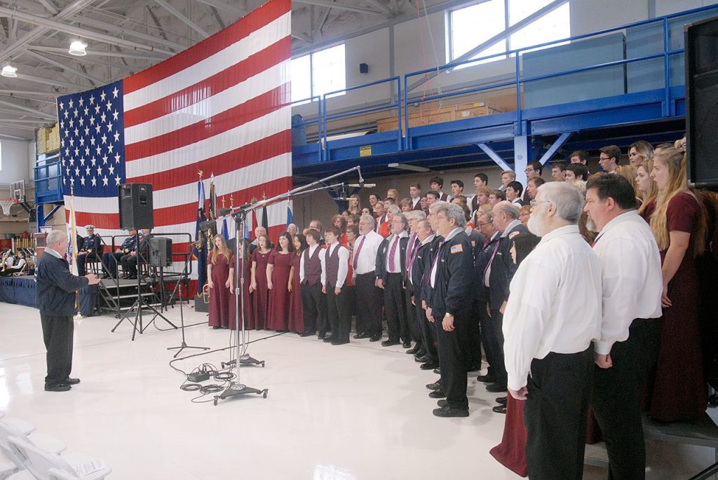 A combined chorus consisting of members of the Olympic Peninsula Men&rsquo;s Chorus, The Grand Olympics Chorus of Sweet Adeline&rsquo;s International, Mix Up A Capella and the Sequim High School Select Choir perform under the direction of Jim Davis during last Friday&rsquo;s Veterans Day ceremony in the hanger of U.S. Coast Guard Air Station/Sector Field Office Port Port Angeles. (Keith Thorpe/Peninsula Daily News)