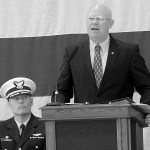 Keith Thorpe/Peninsula Daily News Retired U.S. Coast Guard Rear Admiral Richard Gromlich, right, delivers the keynote address during Friday&rsquo;s Veteran&rsquo;s Day ceremony in the hanger of U.S. Coast Guard Air Station/Sector Field Office Port Port Angeles. Looking on at left is Cmdr Mark Hiigel, commanding officer of the station.