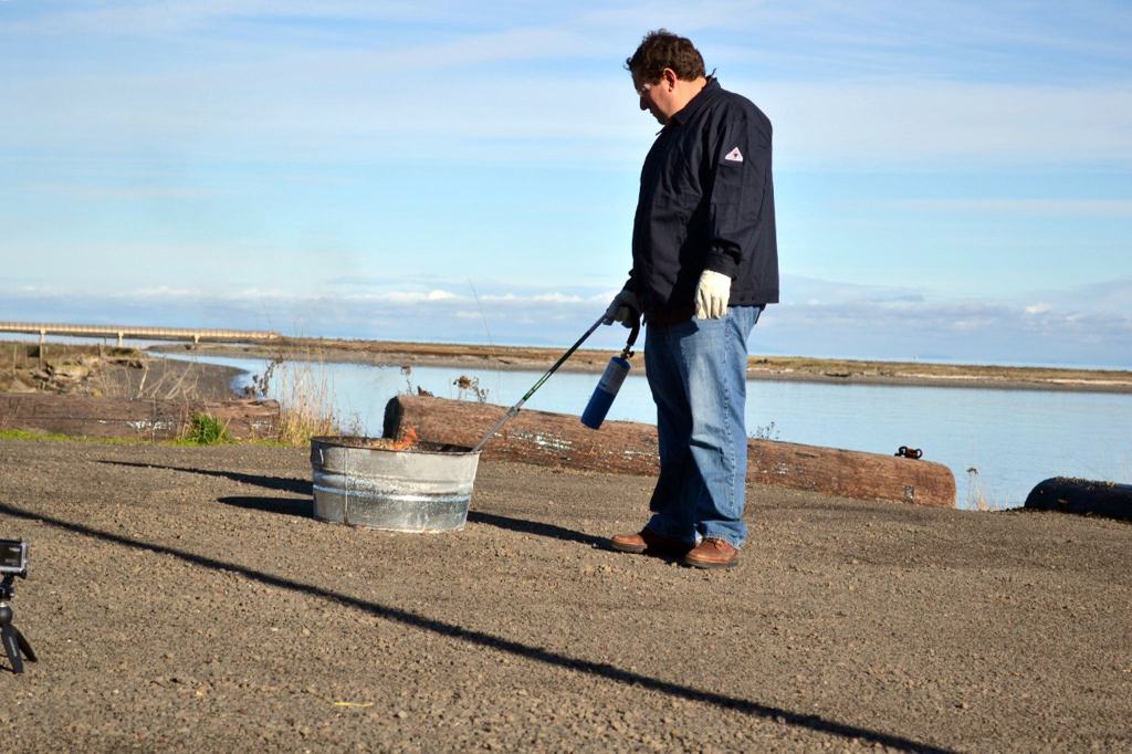 Scientist Robert Jeters, project manager for the Pacific Northwest National Laboratory&rsquo;s aggregator product, uses a propane burner to light an oil slick on fire during a recent demonstration. Sequim Gazette photo by Matthew Nash