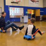 Brent and his son Corbyn Lovell, 6, a first grader at Helen Haller Elementary, ride scooter boards to get their heart rate and step count up as part of a new program, Heart Tech Plus, that monitors that for the students while they participate in physical education. Sequim Gazette photo by Matthew Nash