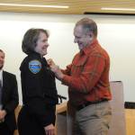 Pat Crain pins the Sequim police chief badge on his wife Sheri after she was sworn into office on Dec. 16. Sequim City Manager Charlie Bush, left, chose her without an interview process following the retirement of Bill Dickinson earlier in December. See story, A-7. Sequim Gazette photo by Michael Dashiell