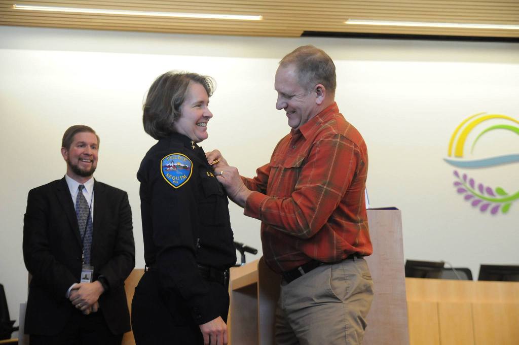 Pat Crain pins the Sequim police chief badge on his wife Sheri after she was sworn into office on Dec. 16. Sequim City Manager Charlie Bush, left, chose her without an interview process following the retirement of Bill Dickinson earlier in December. See story, A-7. Sequim Gazette photo by Michael Dashiell