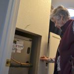 Carolyn Crane of Sequim stands by her furnace where a scammer attempted to charge her $1,500 to remove a dirt clod he likely placed inside. Crane and others report of several recent attempts to scam people for false heating services. Sequim Gazette photo by Matthew Nash