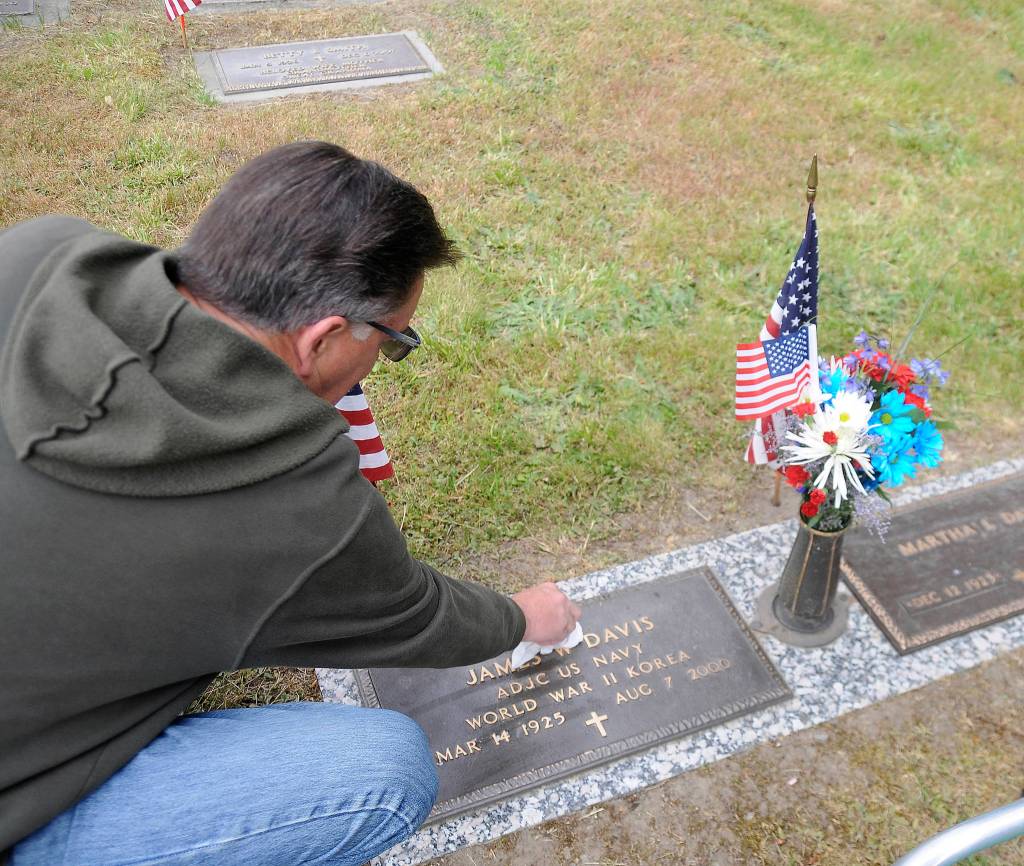 Kimball Shelley of Sequim cleans off the marker for his father-in-law, veteran James Davis. Kimball and Marilyn Shelley said Davis spent his career in the U.S. Navy and helped rescue downed pilots in the Aleutian Islands during World War II. Sequim Gazette photo by Michael Dashiell