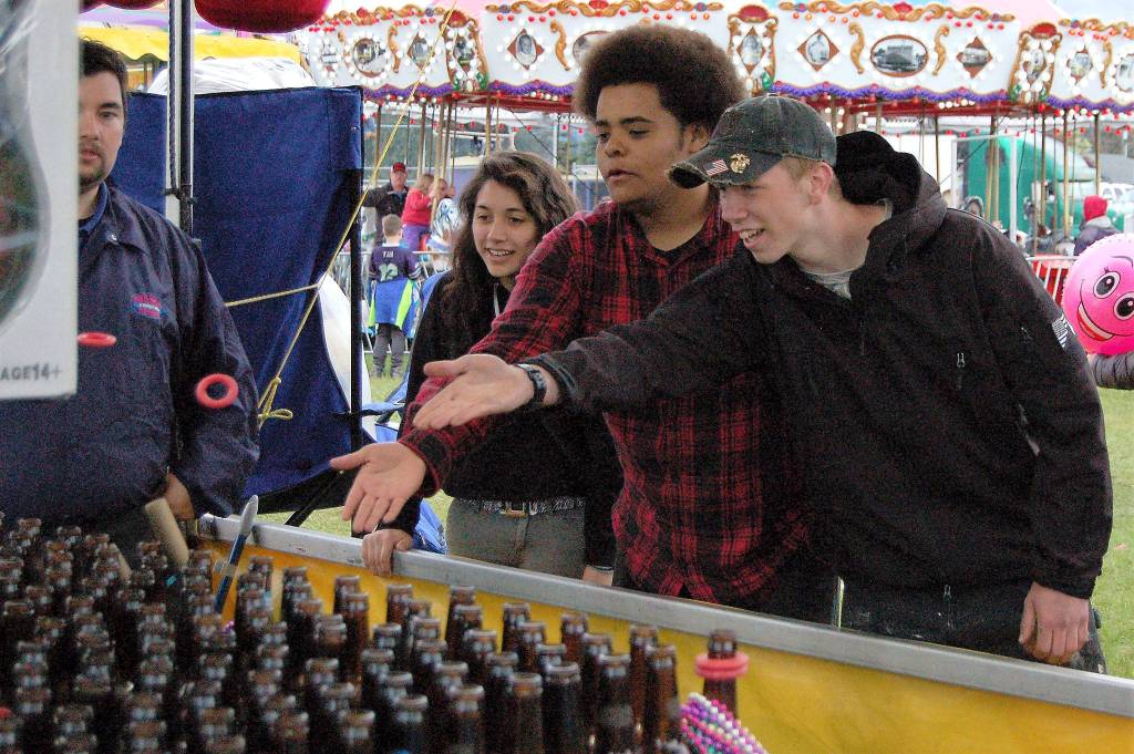 Sequim friends, from left, Anna Laurie, Trevor Jones and Payton Gagnon, all 18, enjoy a round of ring toss at the Sequim Irrigation Festival&rsquo;s carnival on Saturday. It was Gagnon&rsquo;s first time at the carnival, he said, and they all had fun. Sequim Gazette photo by Matthew Nash