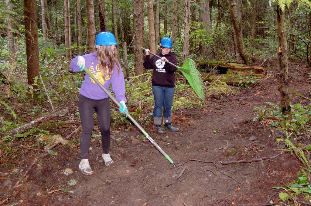 Sequim High freshmen Kjirstin Foresman, left, and Mazie Whitteker, use rakes to clear debris from a new trail they and other high schoolers worked to build on Miller Peninsula from May 2-4. They learned about sharing the trail with bicyclists and stock, careers in forestry management and about different tools for clearing trails. Sequim Gazette photo by Matthew Nash