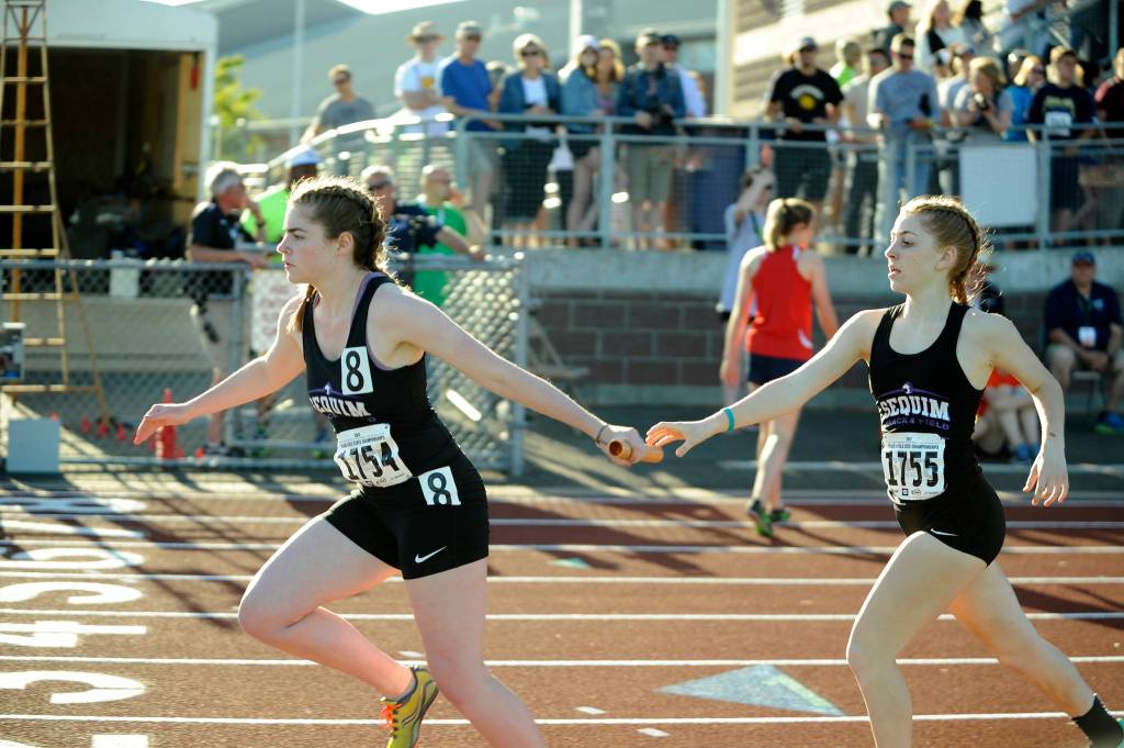 Sequim&rsquo;s Rylee Gray, left, gets a handoff from teammate Daisy Ryan in the anchor leg of the 4x400 relay on May 25. Sequim Gazette photos by Michael Dashiell