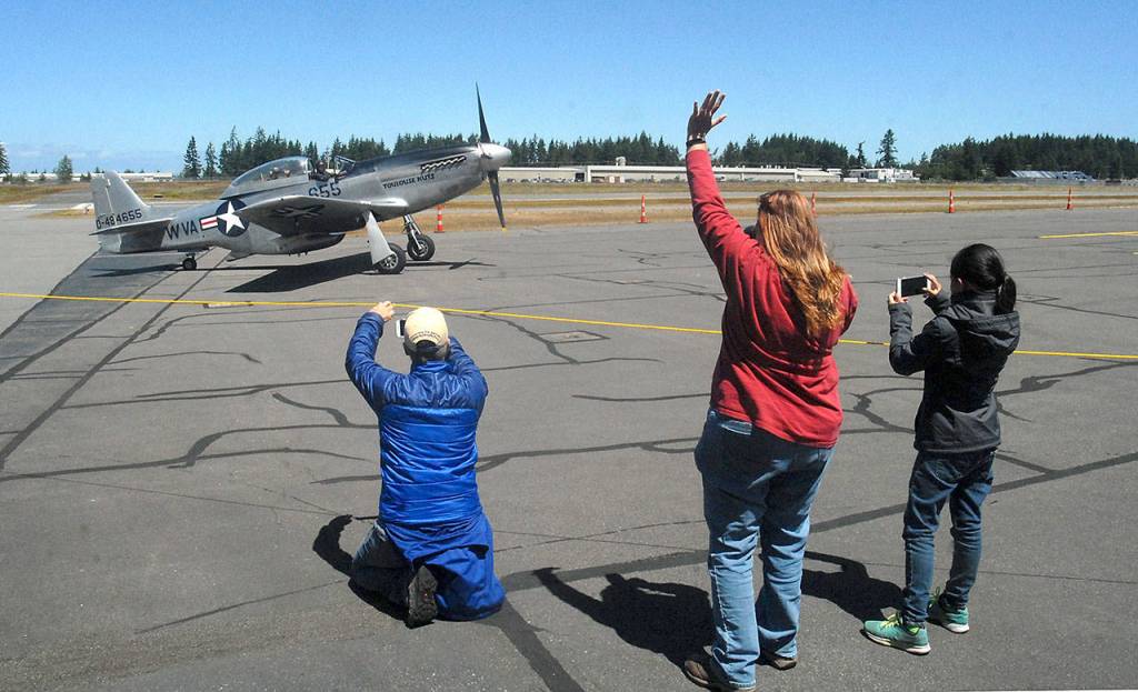 Ricki McLaughlin of Port Angeles, center, waves at the arrival of a vintage TF-51D Mustang as Kelly Thomas of Sequim, left, and Jenna McGoff, 13, of Port Angeles take photos. (Keith Thorpe/Peninsula Daily News)