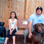 Alabama and her dad Kevin Cassidy sit on a bench with their dog Remington last October that memorializes family dog Stolli, who died on Aug. 31, 2016. The statue to the left was reported stolen Aug. 3 and recovered later in the day broken. Community members look to fund a replacement for the Cassidy family. Sequim Gazette file photo by Matthew Nash
