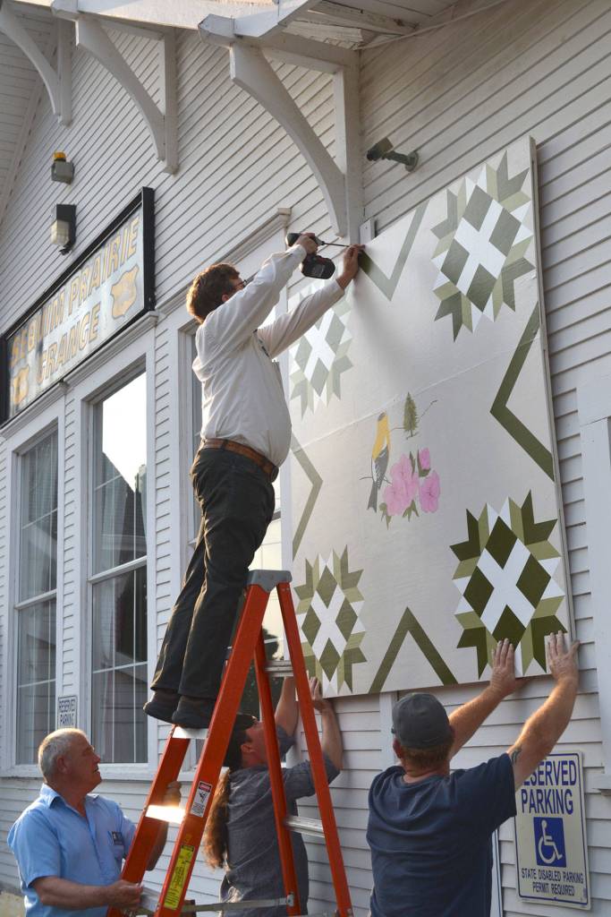 Volunteers attach a 6-foot by 6-foot Barn Quilt on Aug. 12, 2015, on the side of Macleay Hall as part of the Washington State Heritage Quilt Trail. It&rsquo;s one of 16 quilts on display in Washington. Sequim Gazette file photo by Matthew Nash