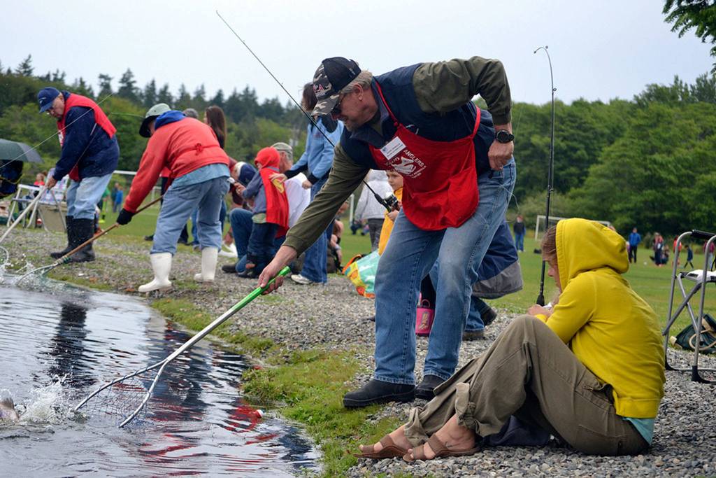 Jamie and Gibson Hill of Sequim pull in a fish while Dave Dewald tries to net it at Kids Fishing Day in 2016. Organizers of the event plan to hold it again the third Saturday in May 2018, but they move the event to another pond in 2019 to preserve the fish from hot weather. Sequim Gazette file photo by Matthew Nash