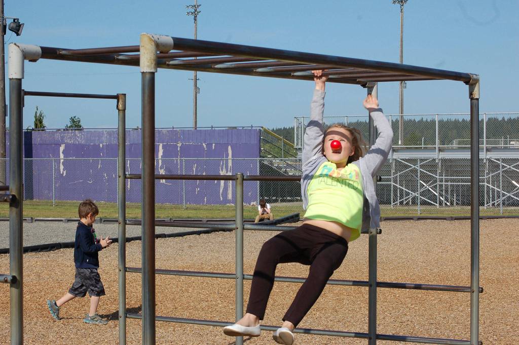 Paige Penson, a fourth grader at Helen Haller Elementary School, swings across the monkey bars wearing a red nose to complete the Ninja Warrior course during the Boys and Girls Clubs red nose day on May 24. Sequim Gazette photo by Erin Hawkins
