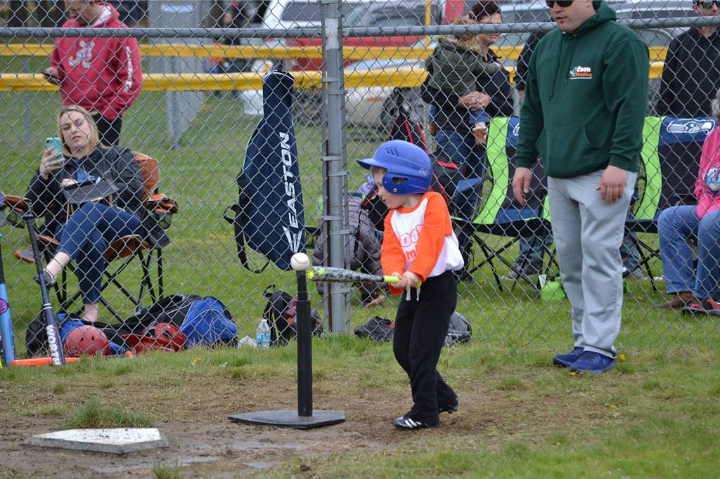 Reed Nash takes a swing as T-ball coach John Coon looks on during a game earlier this season. For many players, it was their first experience on a team sport. Sequim Gazette photo by Matthew Nash