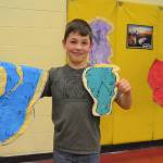 Noah Andrzejeski, 9, from Rachel Odens third grade art class stands with his pieces following the style of Salvador Dali. Noah said he likes the colors and how the clocks melt and droop.