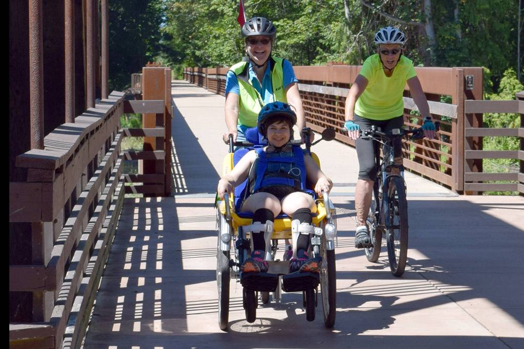 Sequim Wheelers volunteer Elaine Cates pilots a wheelchair bike with Clallam Mosaic participant Kaitlyn Winn, foreground, and Sequim Wheelers volunteer and safety Michele Fraker, right, at Railroad Bridge Park. Submitted photo