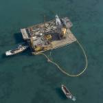 Crew members from Quigg Bros. use a crane to take a creosote piling from Dungeness Bay before loading it into a barge loaded with pieces from the old Dungeness wharf. Photo by John Gussman