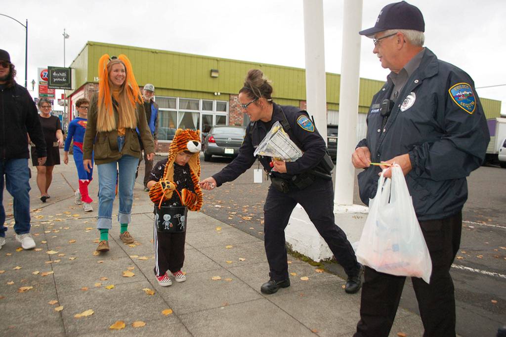 Sequim Police Officer Kindryn Leiter, left, and volunteer officer Larry Smith, right, hand George Jarvis, 3, candy as he trick-or-treats with his parents in downtown Sequim on Oct. 31. Sequim Gazette photo by Erin Hawkins