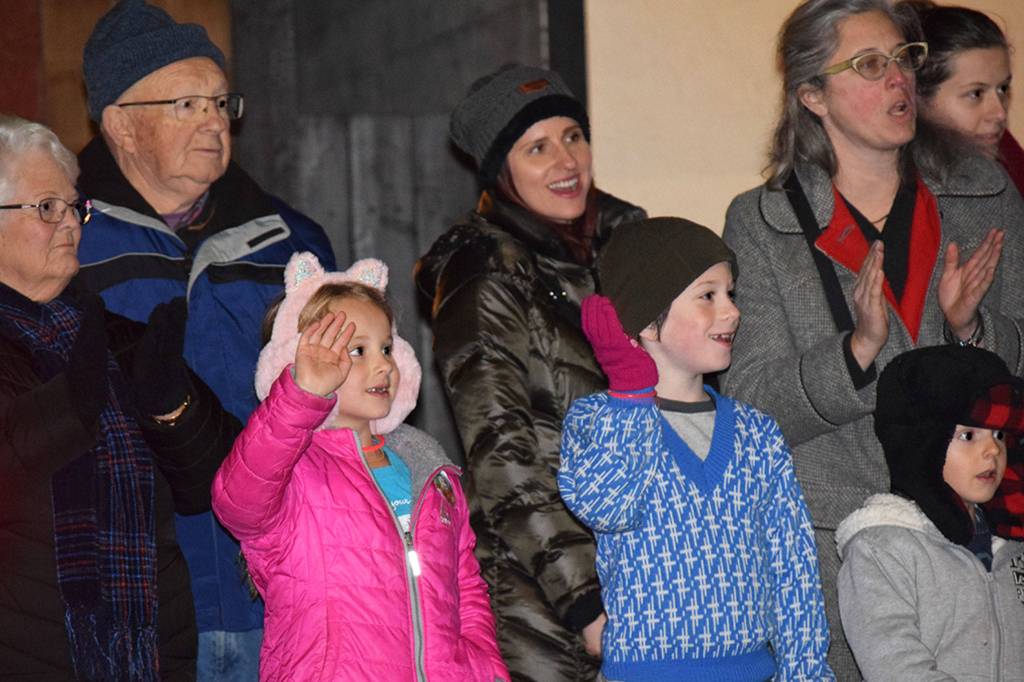 Evie Hall, front left, Nicholas Breitbach, and Tommy Hall, wave as tractors decked out in Christmas attire drive down East Washington Street on Nov. 24. Sequim Gazette photo by Erin Hawkins