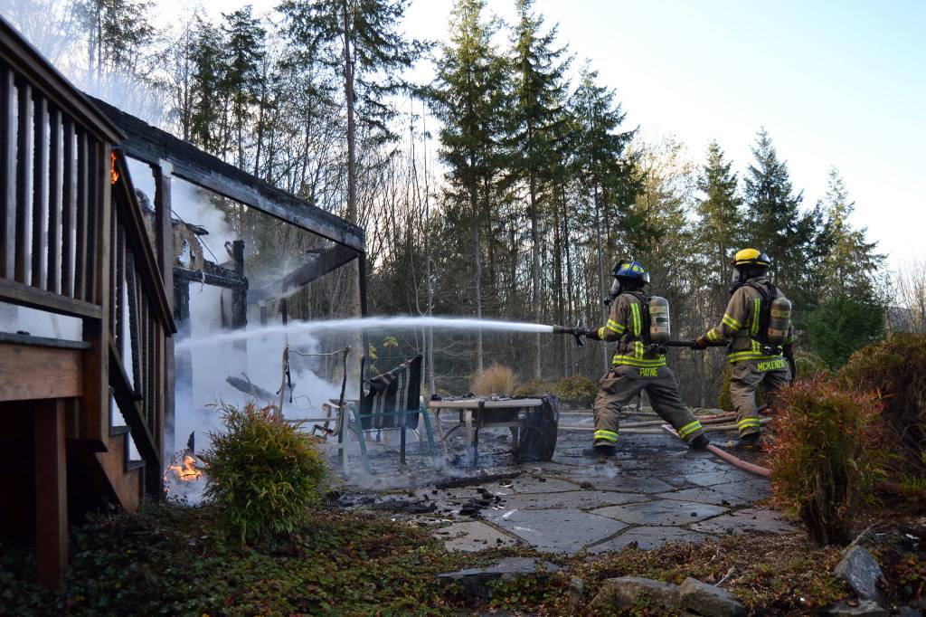 Firefighter/Paramedic Erik Payne and Firefighter/EMT John McKenzie battle flames on a Blyn homes deck on Monday. Sequim Gazette photo by Matthew Nash