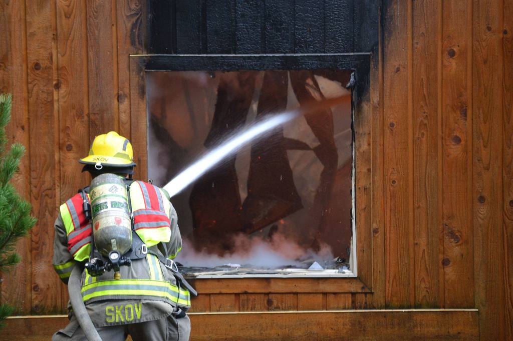 Firefighter/EMT Kjel Skov sprays the inside of a deck spanning from a house fire that erupted on Monday morning in Blyn. Sequim Gazette photo by Matthew Nash