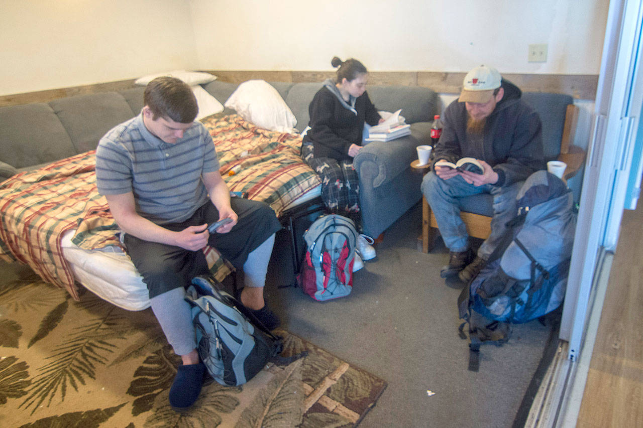 Jacob Olson, left, looks through Magic the Gathering cards while Colleen and Ted Chapman read at Serenity House of Clallam Countys night-by-night shelter Thursday. The shelter is open 24/7 while temperatures stay below freezing. (Jesse Major/Peninsula Daily News)