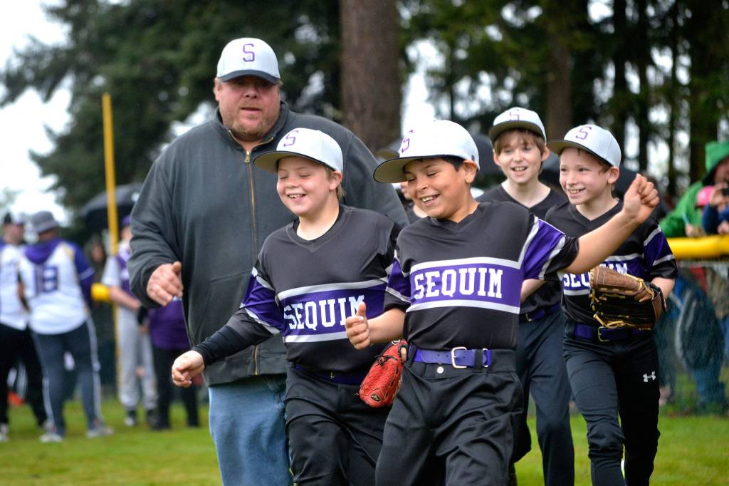 Olympic Game Farm Minor League players, from left, Kaleb Delph, 10, Domink Johnson, 9, Cooper Sharpe, 11, and Brody Lewis, 10, race their coach Quentin Delph during the Sequim Little Leagues Players Procession. Each team was introduced in front of hundreds of spectators at Dr. James Standard Memorial Little League Park.