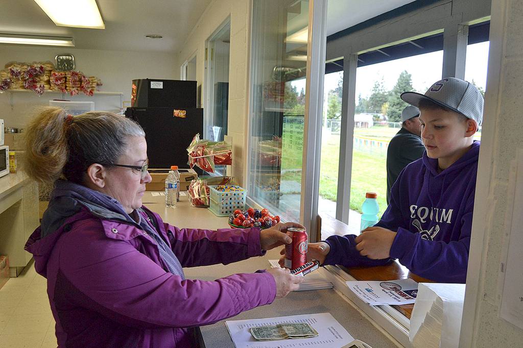 Parent volunteer Jackie Lake helps Charlie Grider, 12, with Evergreen Collisions Boys Majors team, grab a snack from the concession stand after the opening ceremony of the Sequim Little Leagues season. Despite a rainout for games, players received a hot dog, drink and chips courtesy of Molina Healthcare.
