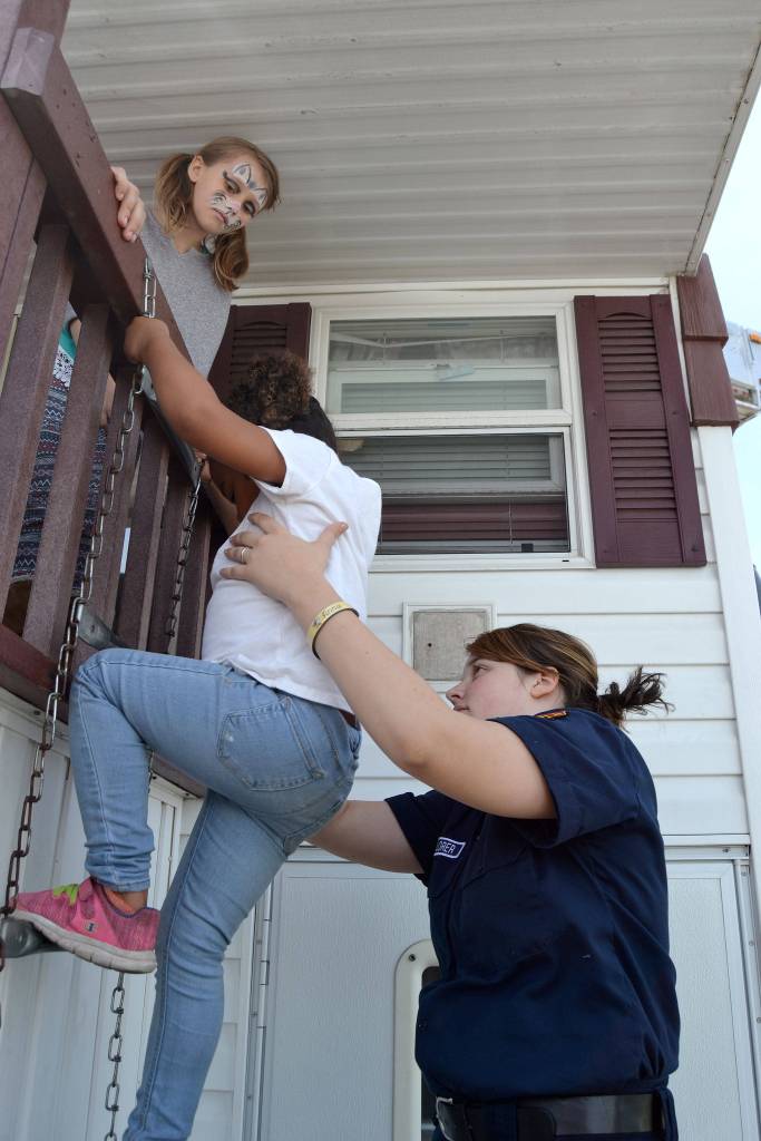 Explorer Scout Anna Fallon, 16, with Clallam County Fire District 3, helps Mya Whiteside, 5, down from a smoke-filled room as Isabella Freitas, 9, waits hurt turn down from the fire safety trailer. Sequim Gazette photo by Matthew Nash